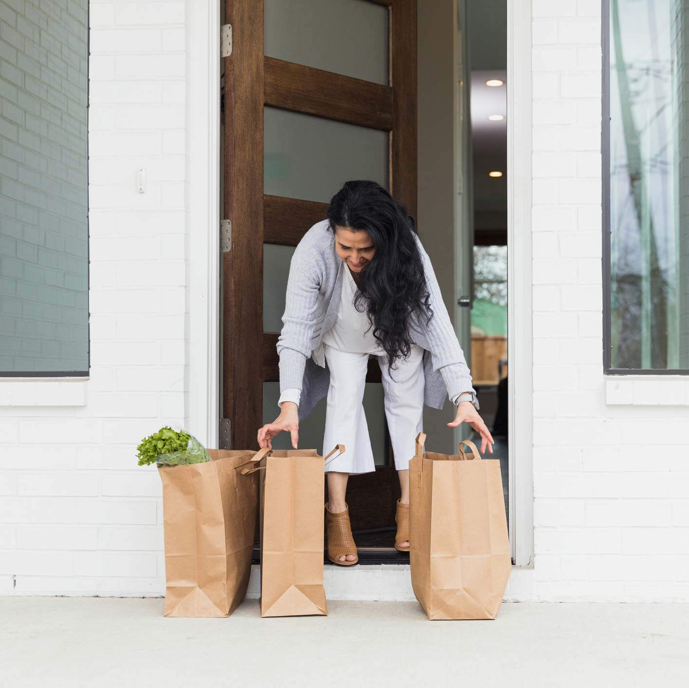 woman picking up grocery bags from from front porch