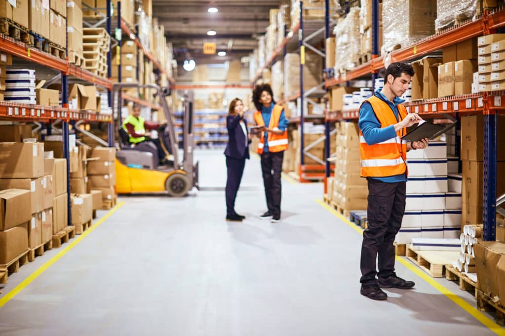 warehouse workers checking tablets in warehouse aisle