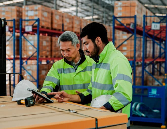 hybrid workers in a warehouse discussing something on an ipad