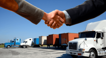 two people shaking hands in front of semi trucks